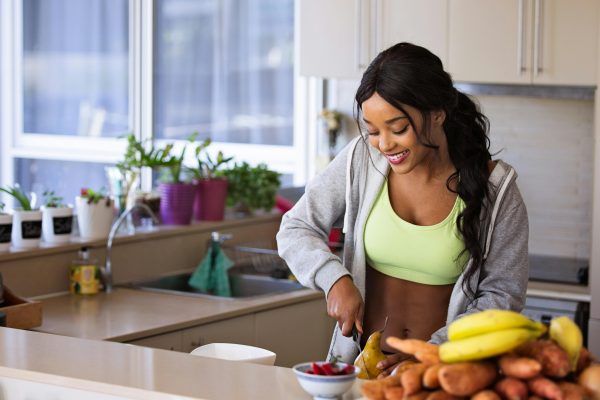 Honeyerries Fit a Healthy Lifestyle Smiling woman preparing fresh fruit in a sunlit kitchen, embodying a healthy lifestyle.